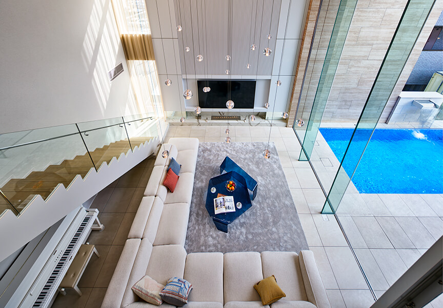 BOCCI のペンダントライトが浮かぶ、高級住宅のリビングデザイン。吹き抜けの空間に大開口を備え、プールを借景する